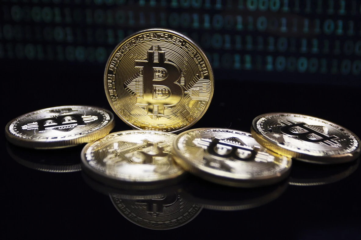 Pięć złotych monet z symbolem bitcoina na ciemnym tle